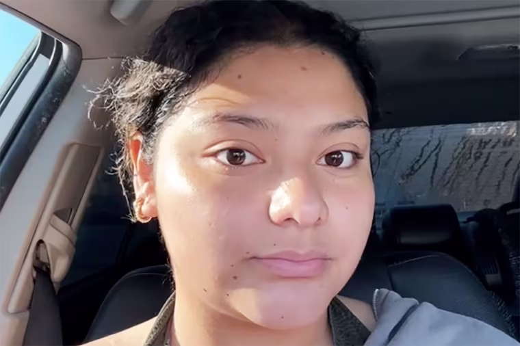 Close-up of a person seated in a car looking straight at the camera with a neutral expression.
