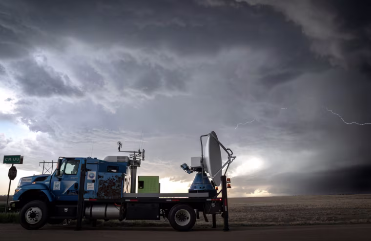 Dark storm clouds and lightning with a large truck carrying a satellite and other equipment in its flatbed.