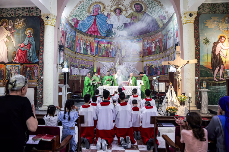 Pierbattista Pizzaballa holds a container with smoke flowing out at the front of the church, people kneel