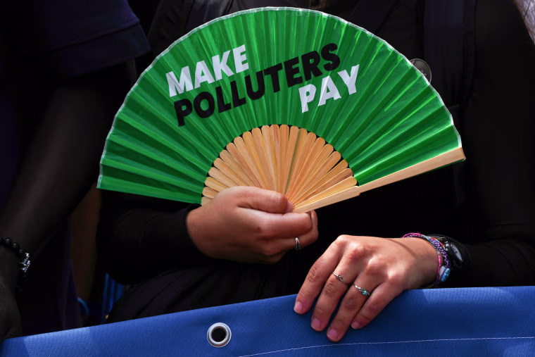 An activist holds a fan that reads "make polluters pay"