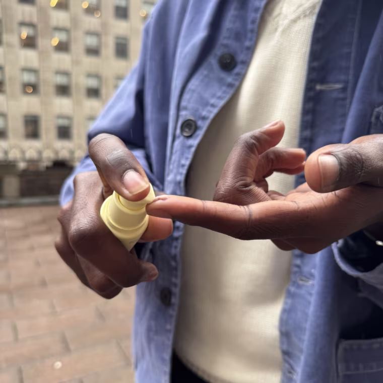 Bowman squeezing the Dr. Loretta sunscreen onto the tip of his finger with a building in the background.