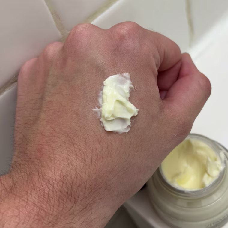 Person holding Bobbi Brown moisturizer and primer container with product on back of hand