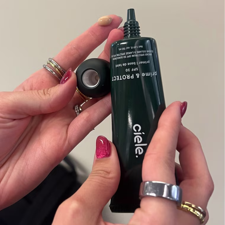 Woman holding Ciele primer packaging with dot of primer on finger