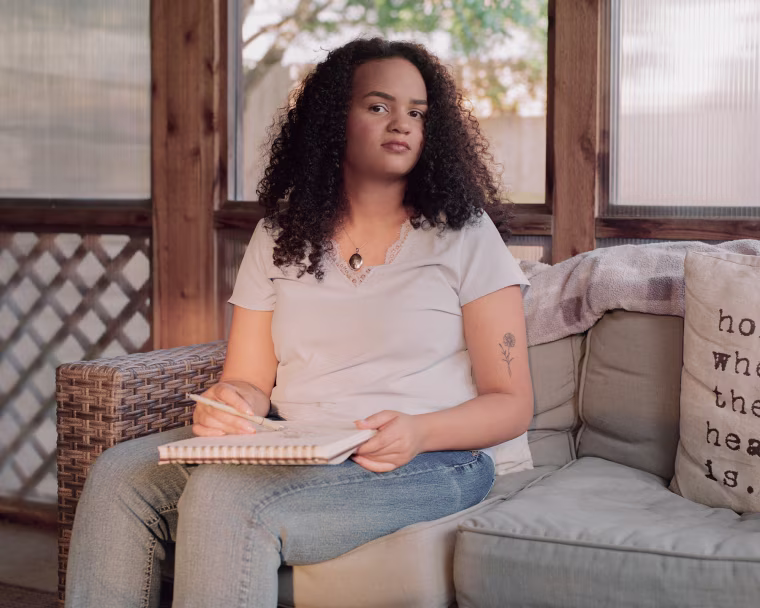 Nala White seated on a couch while holding a drawing pad and a pen