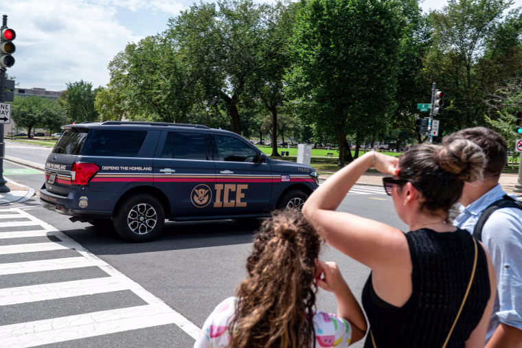 An Immigration and Customs Enforcement police SUV patrols on the road as people watch from the sidewalk