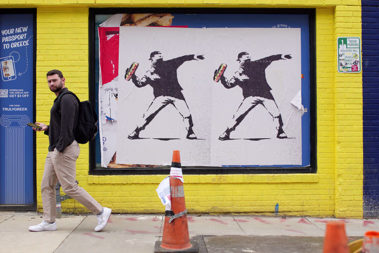 A person walks past Banksy-style posters of a protester throwing a sandwich on Aug. 21, 2025.