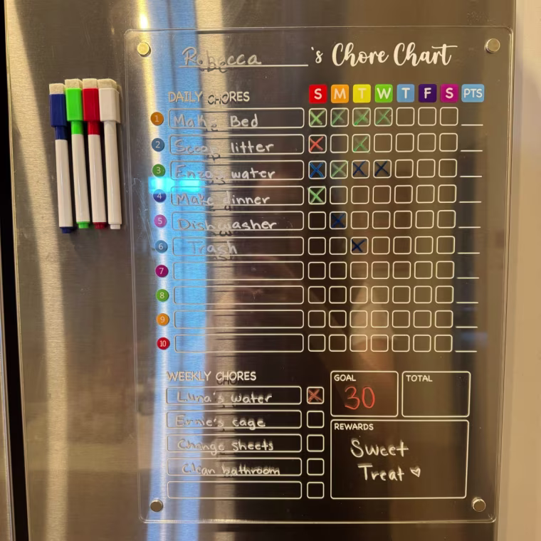 Clear acrylic chore chart magnetized to refrigerator with four markers on the left.