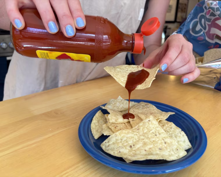 A hand holding a bottle of Valentina Hot Sauce in front of a wood table.