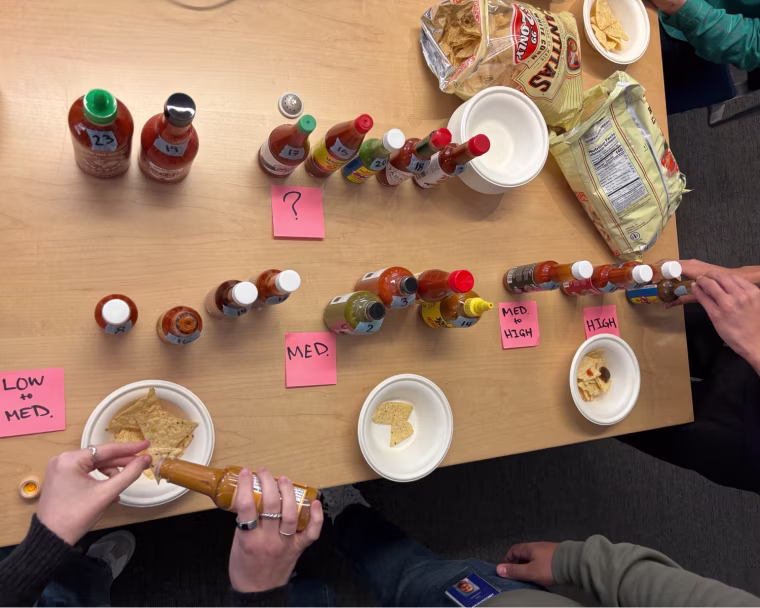 Hot sauces on a wood table with bags of tortilla chips.