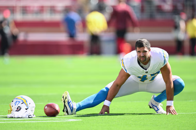 Josh Harris does a squat stretch on the football field next to a football on the ground and his helmet