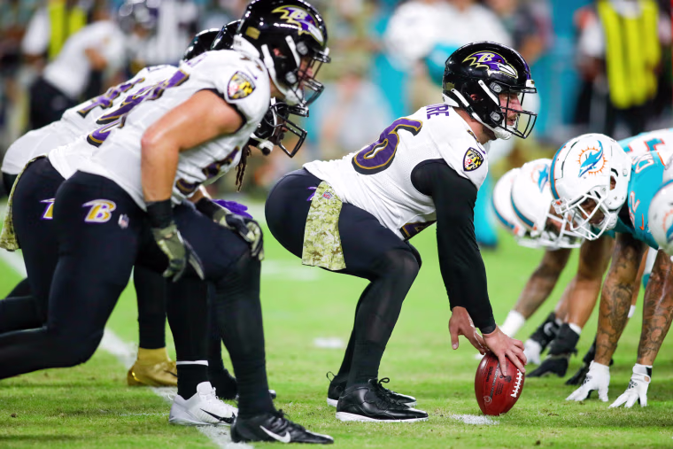 Nick Moore squats and holds the football to the ground in front of a row of his team mates, against a row of opposing team players