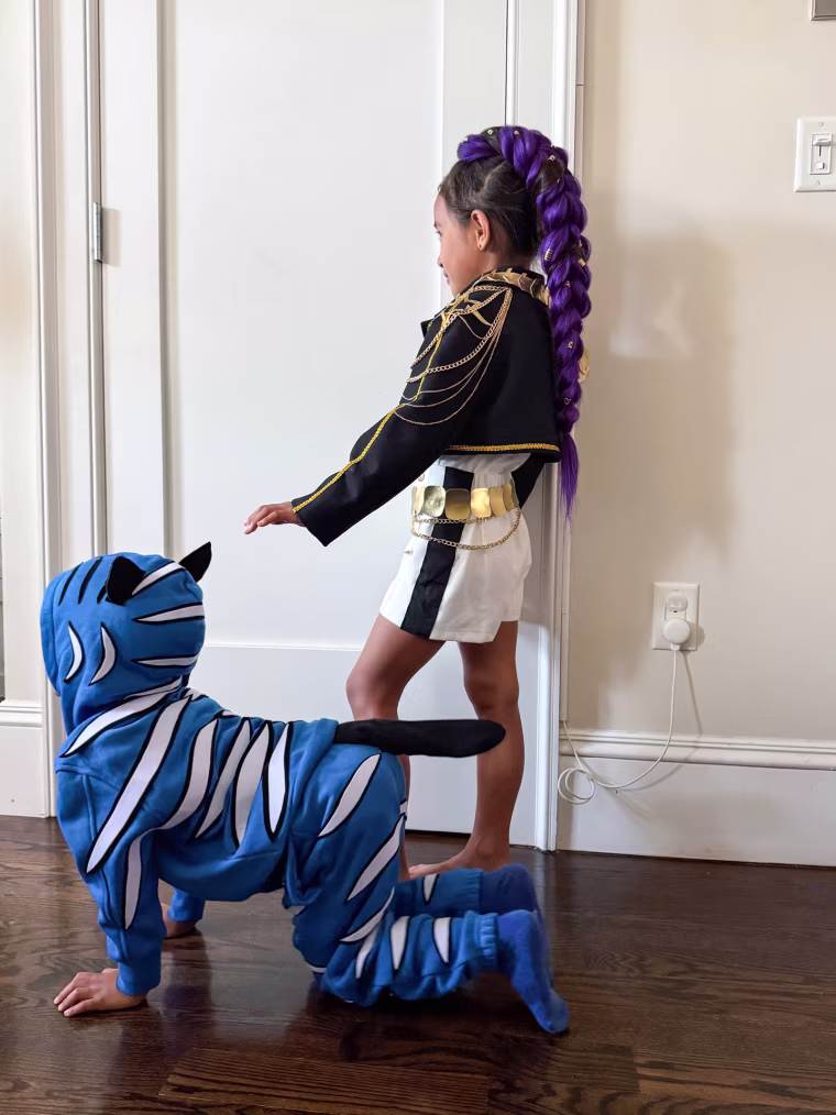 Two children wear Rumi, standing, and Derpy Tiger, crawling on the floor, Halloween costumes