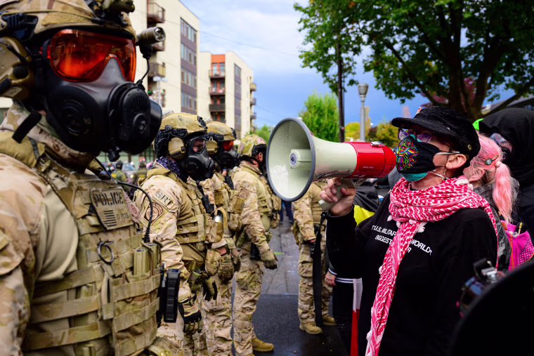 A protester with a bullhorn in front of federal agents.