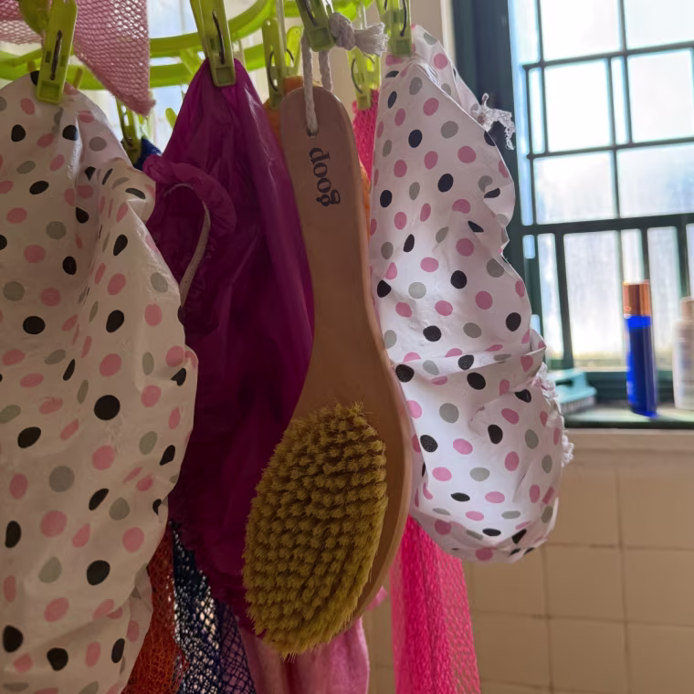 Photo of a wooden brush hanging on a clip and drip hanger in a bathroom.