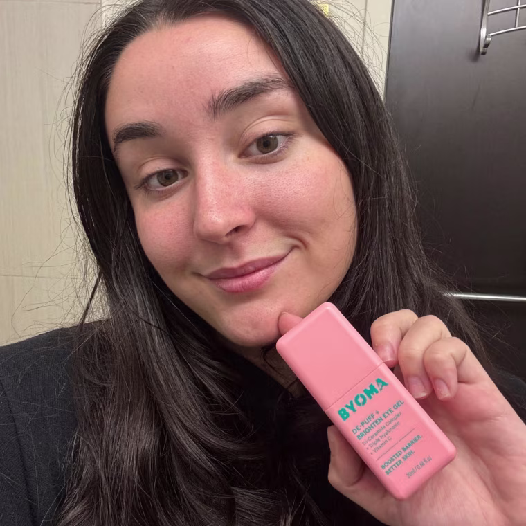 Cusack holding the Byoma Eye Gel in her left hand in front of a wall.