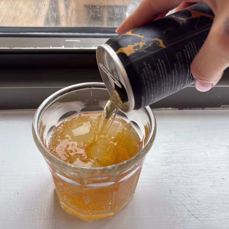A hand pouring a can of Free AF’s Whiskey Ginger into a glass cup.