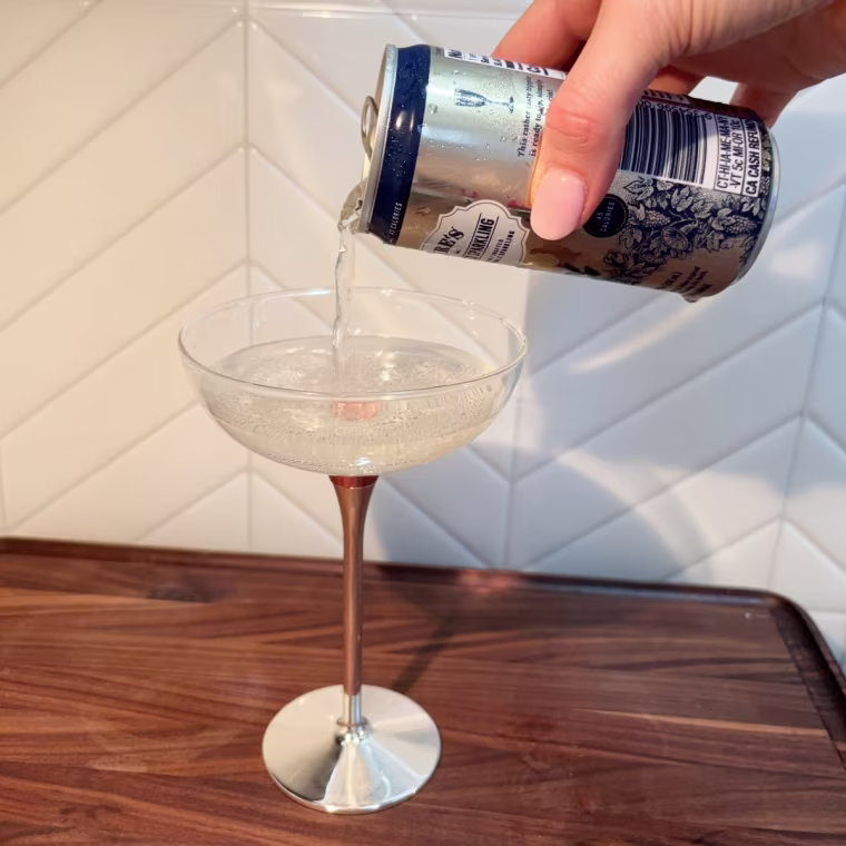 A hand pouring a can of Lyre’s Classico Sparkling into a glass.