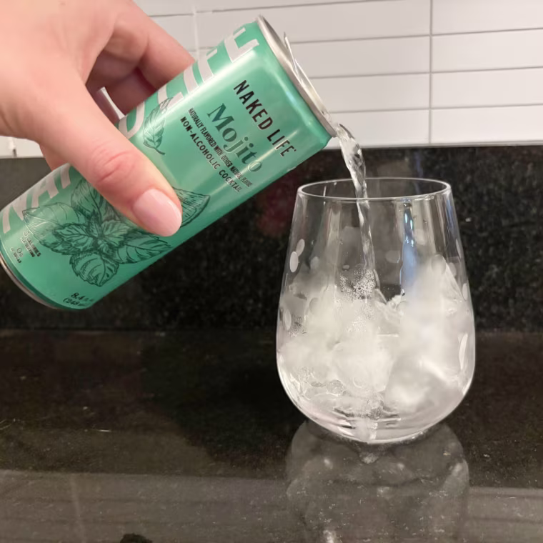 A hand pouring Naked Life’s Mojito into a glass cup.