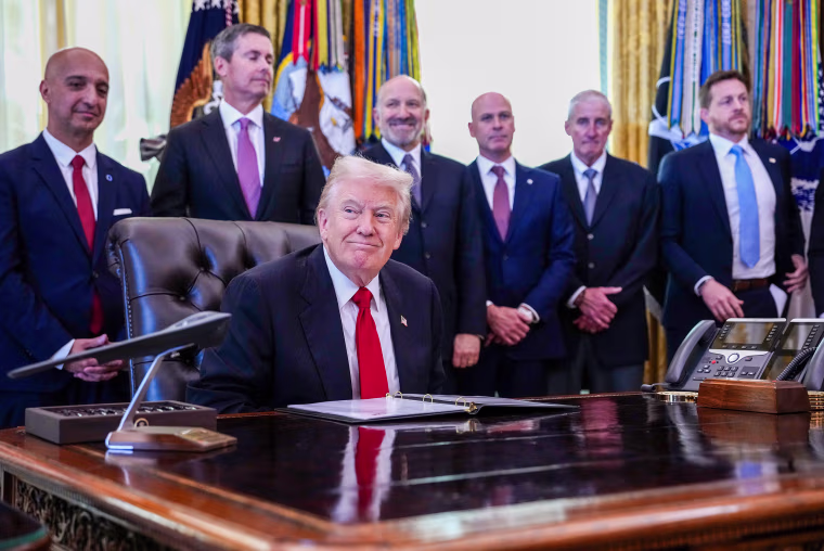 President Trump sits at his desk at the White House surrounded by others.
