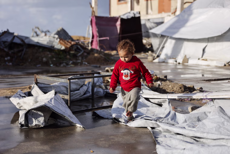 A toddler walks outside on destroyed tent material