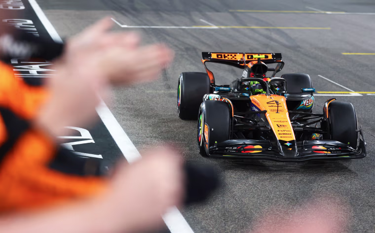 A race car on a race track, hands clapping can be seen on the side of the frame