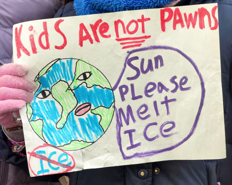 A pink gloved hand holds a sign that reads "Kids are not pawns" with a drawing of the Earth underneath, with a speech bubble that reads "Sun please melt ICE", and the word "ICE" is circled and crossed out in the corner