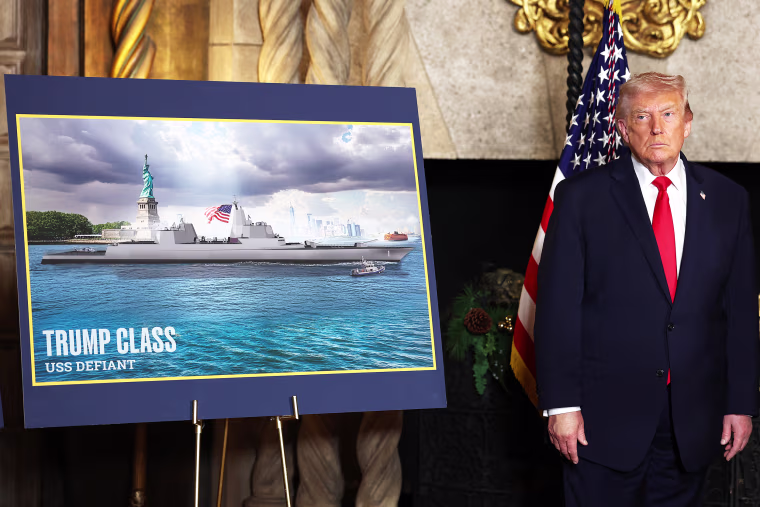 Donald Trump stands next to a signboard with an image of a battleship inside a room at Mar-a-Lago.