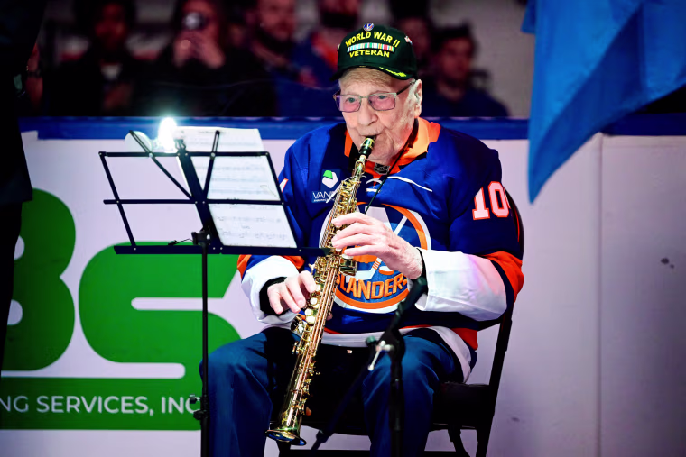 Dominick Critelli plays the clarinet while seated in front of sheet music on a stand, on the ice