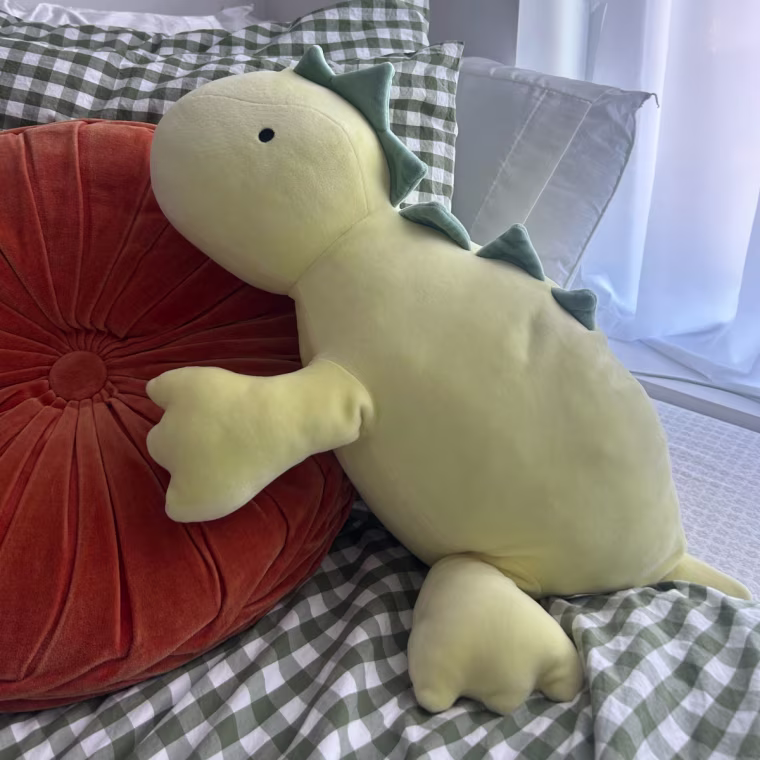 Dinosaur stuffed animal laying on checkered bed sheet