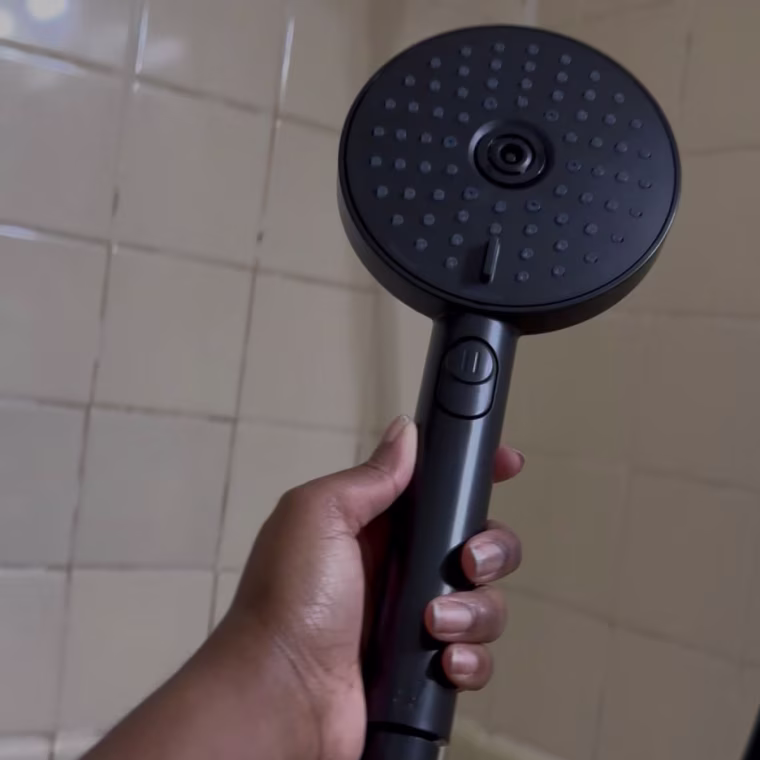 A handheld shower head being held in a bathroom