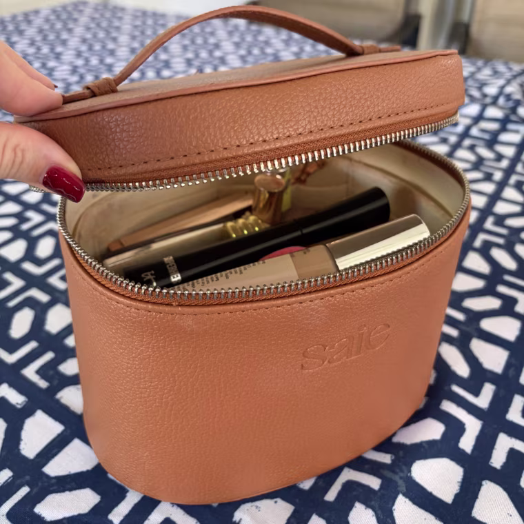 Woman holding open Saie toiletry bag with makeup inside