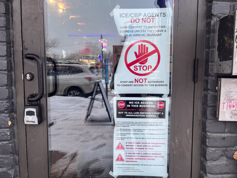 Signs against ICE agents on a storefront door as seen from the outside