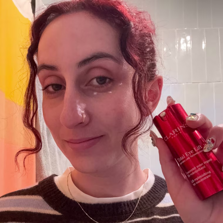 Woman wearing an eye cream while showing packaging