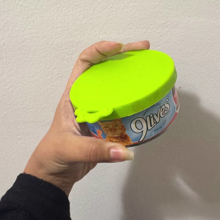 Photo of a hand holding wet cat food with a Comtim Silicone Can Lid against a white wall.