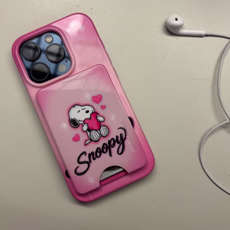 iPhone 15 Pro on table with pink phone case featuring Snoopy holding a heart in airbrush design.