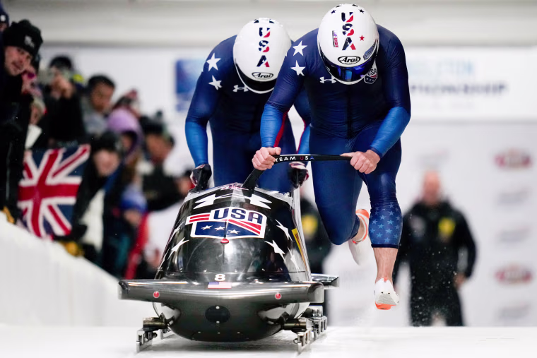 Frank Del Duca and Charles Volke push a bobsled on an ice track next to an audience