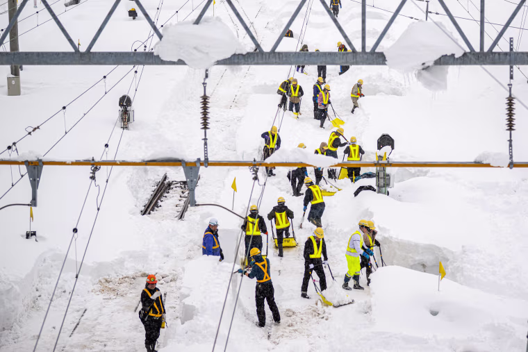 Staff members shovel snow covered rail tracks at Shin Aomori station.