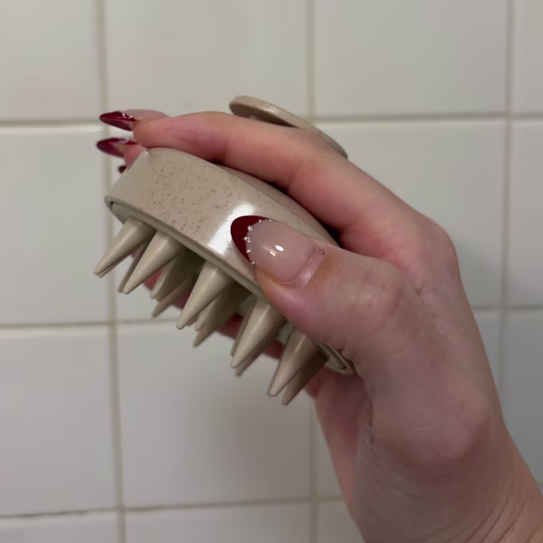 Woman holding a scalp massager against tile wall