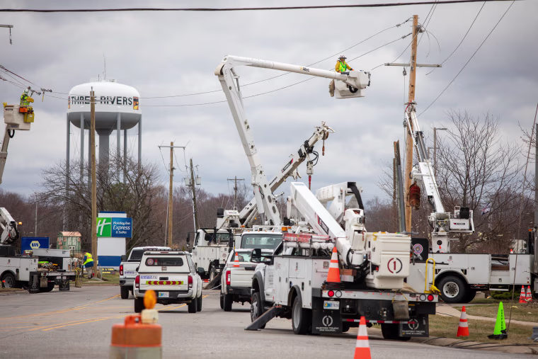 Utility workers in crane baskets work on power lines.