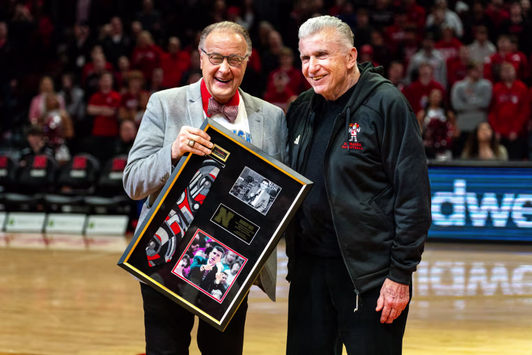 Kent Pavelka, left, and Danny Nee stand on the basketball court and smile for a portrait as Pavelka holds a framed plaque with archival images
