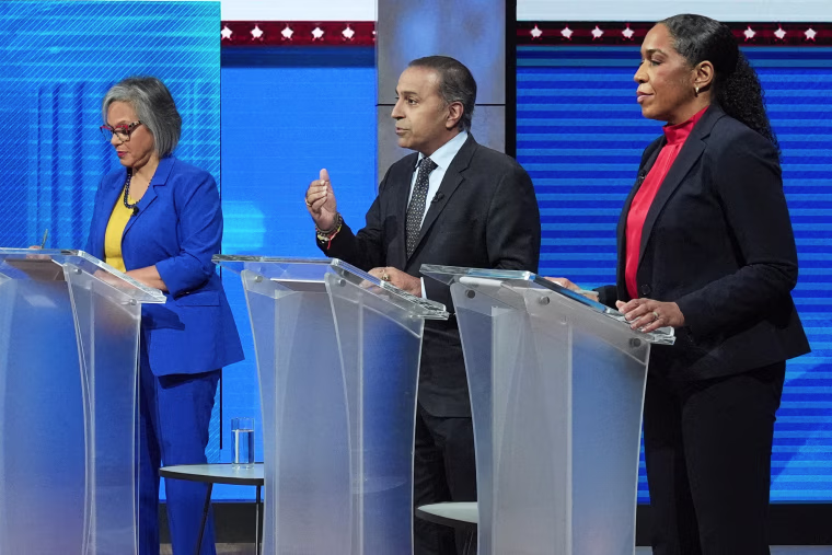 Three politial candidates stand at matching lecterns on a stage during a debate.