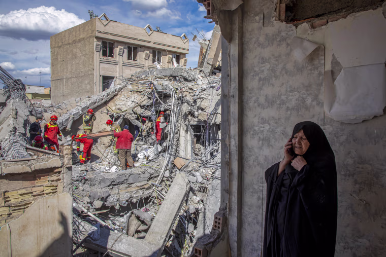 A woman speaks on the phone as emergency workers sift through rubble.