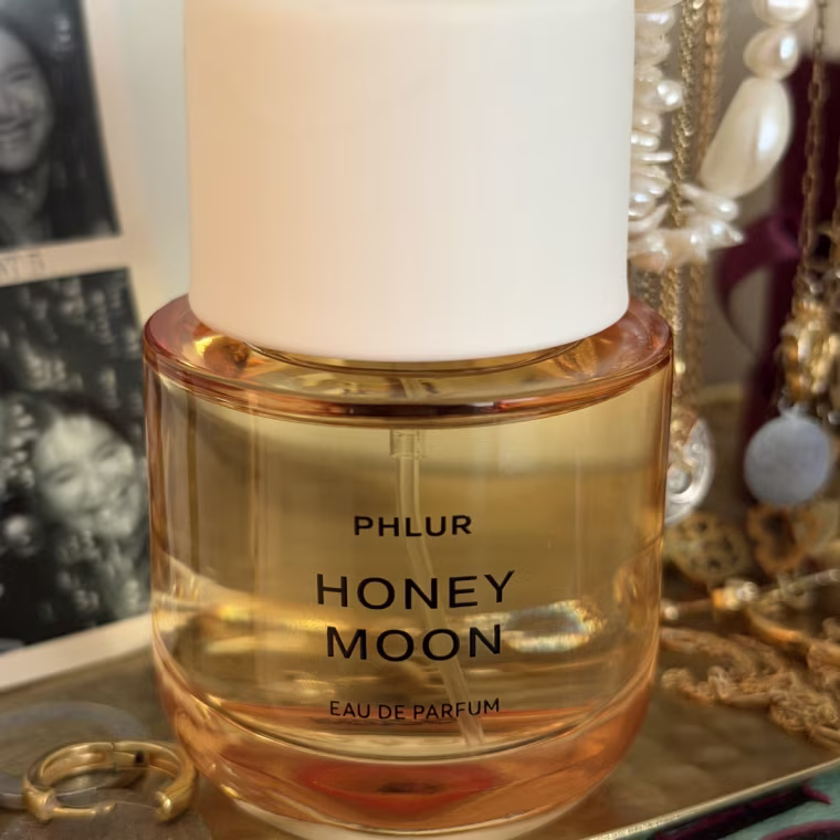 Image of Phlur Honey Moon on a jewelry stand with gold necklaces behind it.