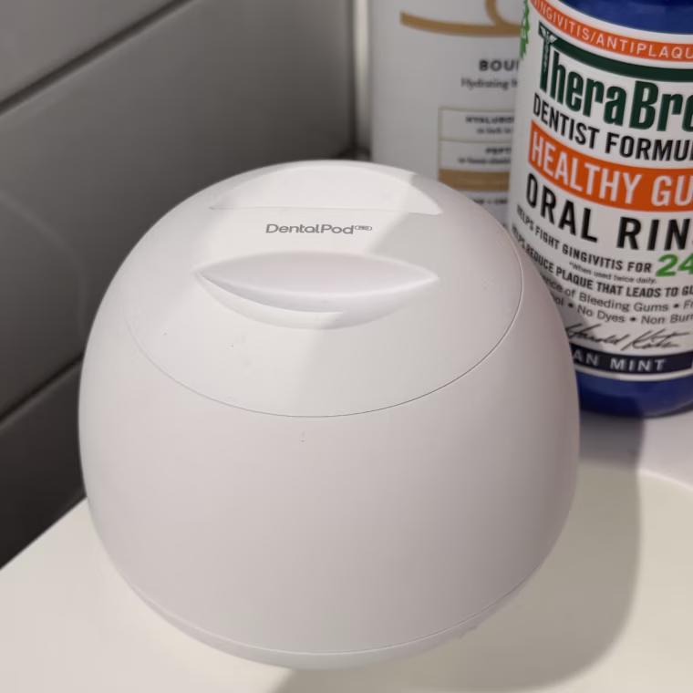 White Zima Dental Pod on a bathroom counter with Therabreath and Billie lotion seen in the background behind it.