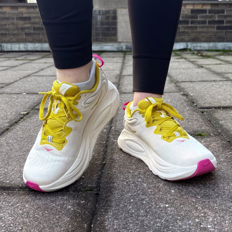 A person wearing yellow Hoka Gaviota 6 sneakers outside.