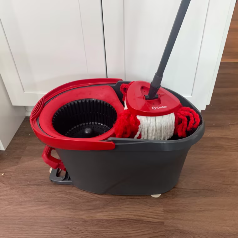 O-Cedar mop bucket sitting on tile floor with mop handle inside.