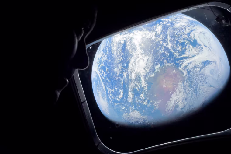 Image: Close up of an astronaut looking out of a spacecraft window with a view of Earth