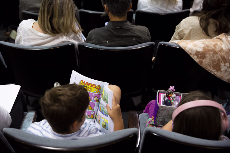 Bridie Lee's son reads a Garfield comic book during an LAUSD board meeting, waiting for his turn to speak in the public comment session.