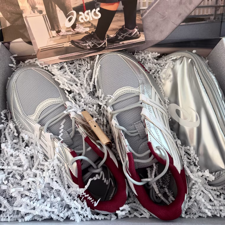 Silver ASICS shoes in a PR box with white confetti.
