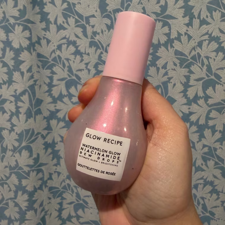 Hand holding the Glow Recipe Watermelon Glow Niacinamide Dew Drops against blue and white flowered wallpaper.